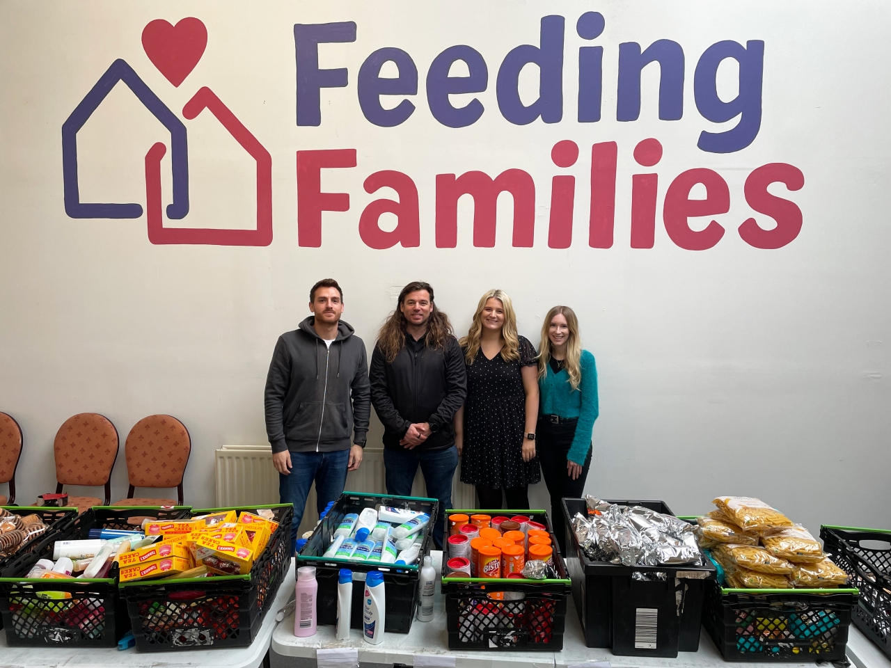 Photo of the team Stood in front of the Feeding Families logo
