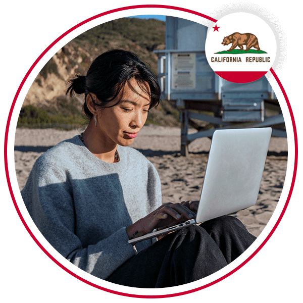 A woman on a beach using a laptop with the california flag overlayed in the top right corner