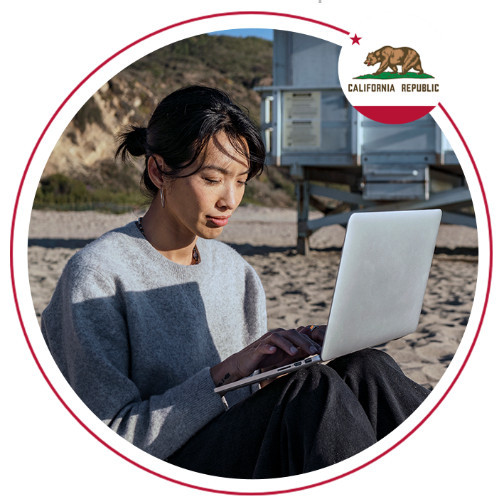 A woman on a beach using a laptop with the california flag overlayed in the top right corner