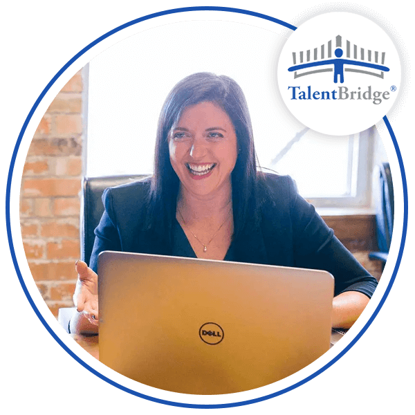 Image of a woman sitting at a desk smiling with her laptop in front of her with the TalentBridge logo above her