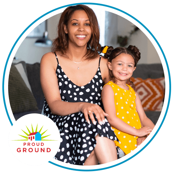 Image of a young woman and a young girl smiling while sitting down on a couch. There is a Proud Ground logo in the bottom left corner