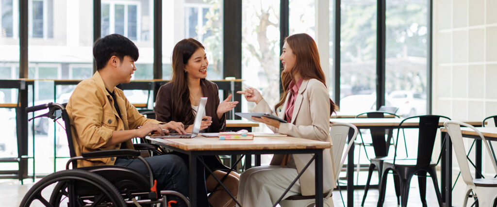 2 women and 1 man in a wheelchair talking in a modern office