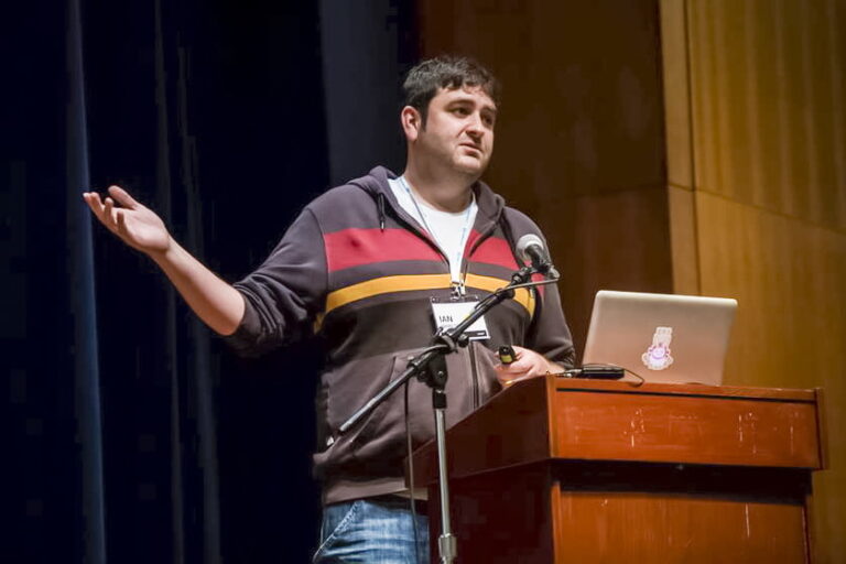 an Hamilton stands in front of a podium and a microphone and laptop.